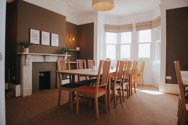 Un comedor con chimenea, sillas de madera y un ventanal con cortinas.