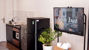 Une cuisine moderne avec un réfrigérateur noir, une plante en pot et un téléviseur à écran plat fixé au mur, qui diffuse de la musique jazz relaxante.