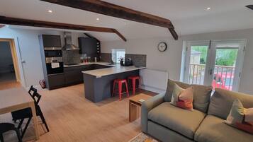 A modern kitchen with a central island, a dining area with a table and chairs, and a living room with a sofa and cushions.