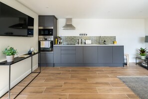 A modern kitchen with grey cabinets, a built-in oven, a stainless steel range hood, and a tiled backsplash. - The Drey Apartment - self-catered Dales luxury (Leyburn)
