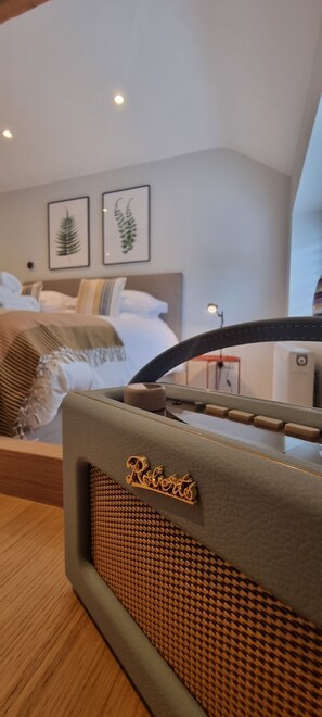 A room with a bed, a mirror reflecting the room, a framed picture on the wall, and a speaker on a table. - The Drey Apartment - self-catered Dales luxury (Leyburn)