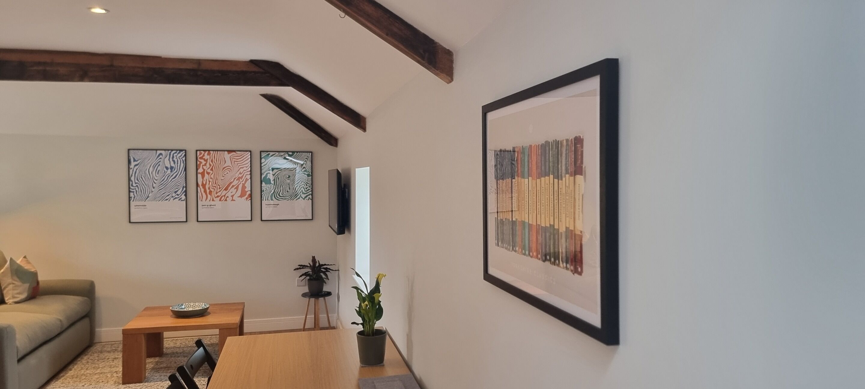 A living room with a wooden table, a sofa, and three framed abstract artworks on the wall.