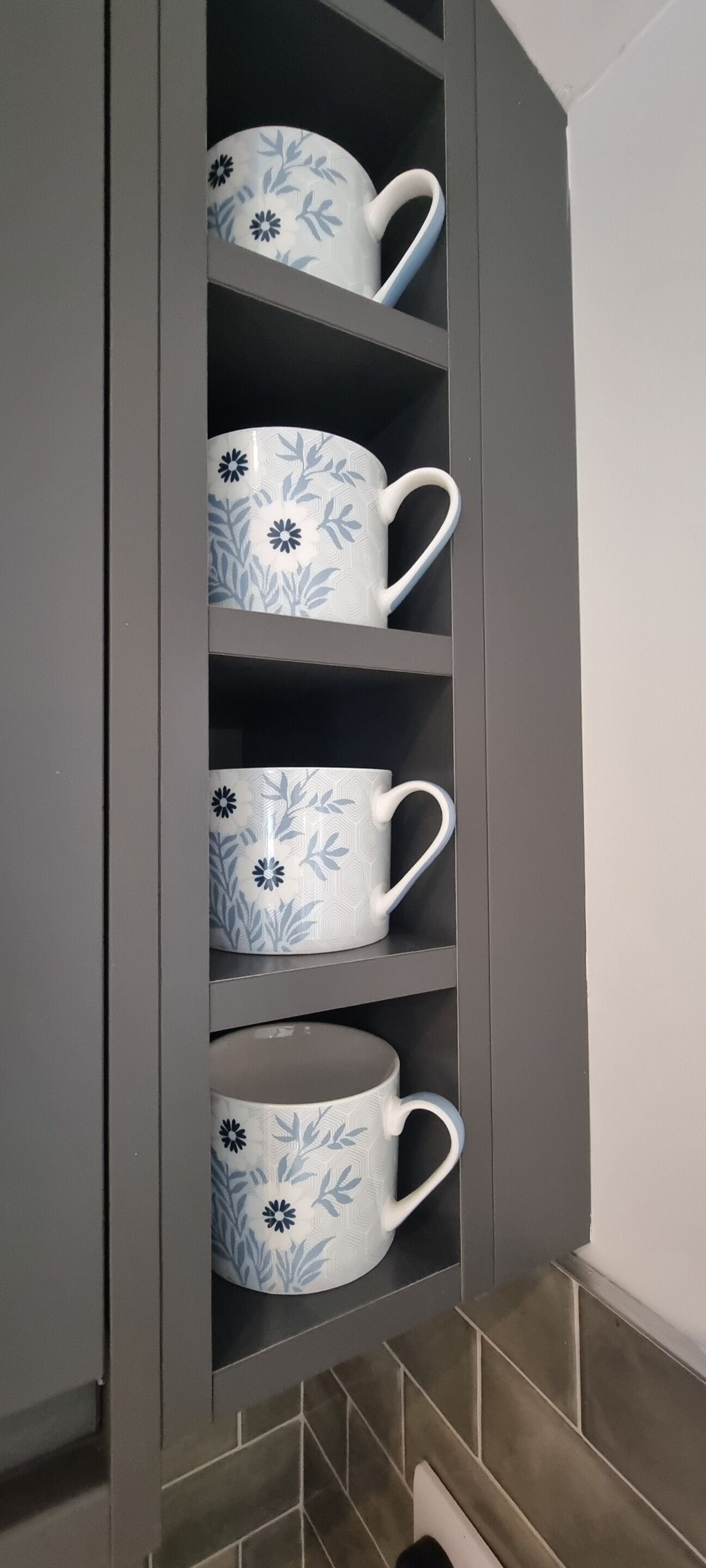 Un mobile grigio con quattro tazze bianche decorate con motivi floreali blu.