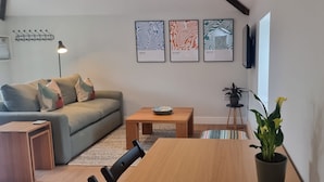 Een woonkamer met een bank, een salontafel, een eettafel en een potplant. Er hangen drie kunstwerken in de wand.