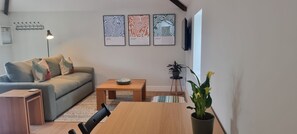 A living room with a sofa, a coffee table, a dining table, and a potted plant. There are three framed artworks on the wall. - The Drey Apartment - self-catered Dales luxury (Leyburn)