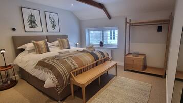 A bedroom with a bed, a bench, a bedside table, a radiator, a window with blinds, and a coat rack.