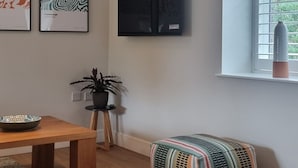 Een moderne woonkamer met een houten tafel, een kleurrijke poef en een raam met uitzicht.