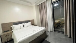 Un dormitorio moderno con una cama grande, una mesita de noche, un vidrio que da a un balcón y vistas de la ciudad.
