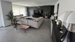 A modern living room with a sofa, coffee table, and a TV. There is a dining area with a table and chairs. - Elegant new 250 m² duplex with garden, swimming pool and spa, a stone's throw from the center of town (Aix-en-Provence)