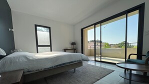 A modern bedroom with a large bed, a small table, and a view of the outdoors through a sliding glass door. - Elegant new 250 m² duplex with garden, swimming pool and spa, a stone's throw from the center of town (Aix-en-Provence)