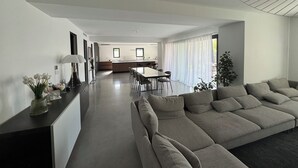 A modern living room with a large sofa, a dining area with a table and chairs, and a kitchen in the background. - Elegant new 250 m² duplex with garden, swimming pool and spa, a stone's throw from the center of town (Aix-en-Provence)