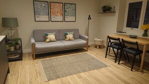Een moderne woonkamer met een grijze bank, twee bijzettafeltjes, een salontafel en een eethoek met stoelen.
