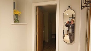 Een hal met een houten deur, een spiegel en een plank met bloemen.