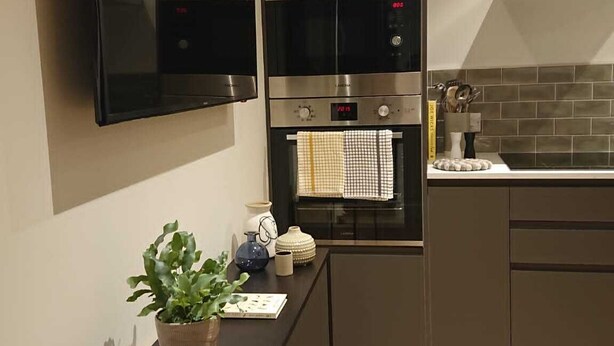 A modern kitchen with a built-in oven, a microwave, and a flat-screen TV mounted on the wall. - Modern Self-catering Apartment - The Holt (Leyburn)