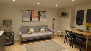 A modern living room with a grey sofa, two chairs, a small table, and a floor lamp. There are three framed artworks on the wall. - Modern Self-catering Apartment - The Holt (Leyburn)