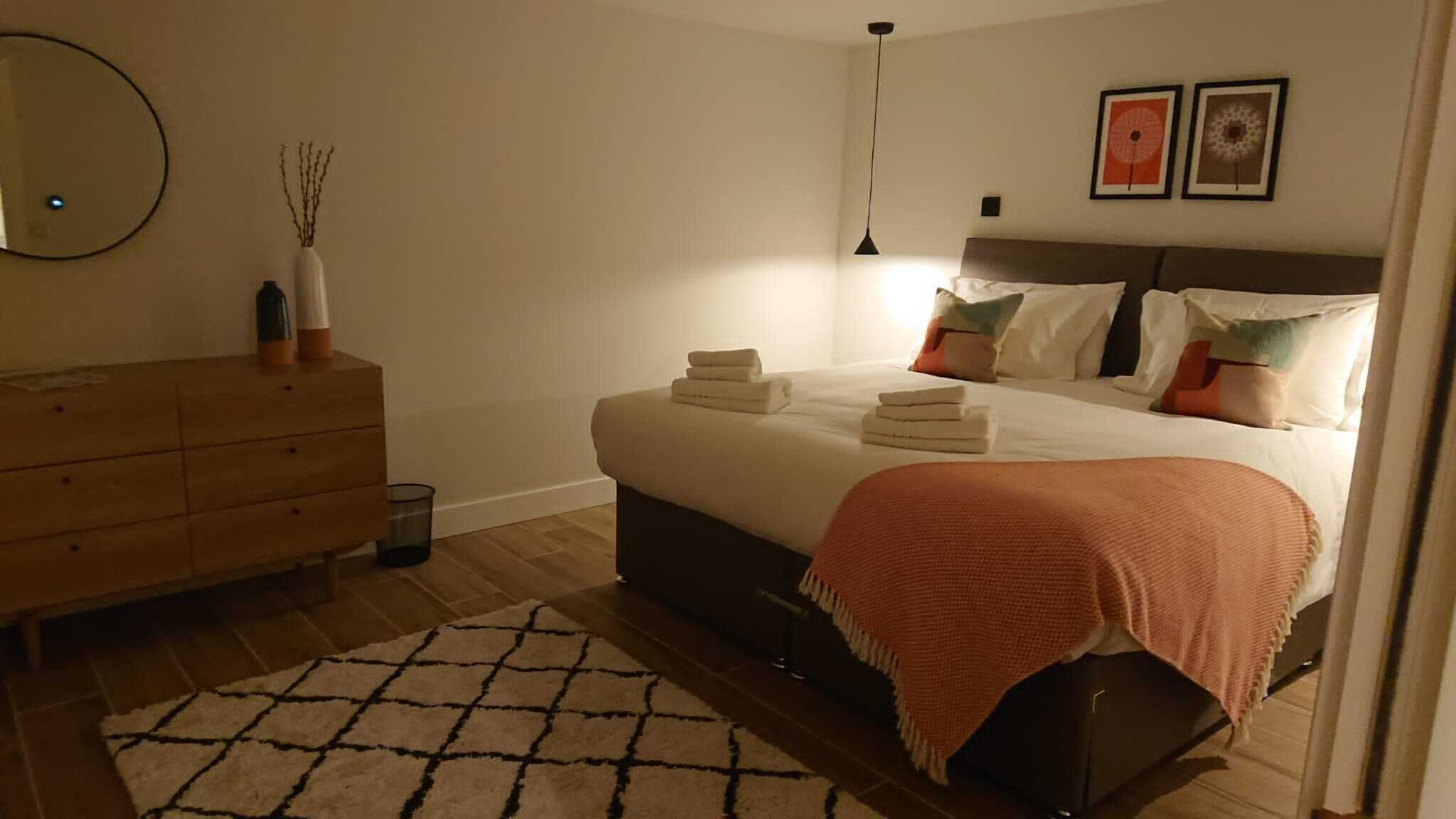 Une chambre à coucher comprenant un lit, des tables de chevet, une commode, un miroir et un tapis.