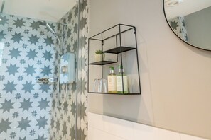 A bathroom with a shower, a mirror, and a shelf with toiletries. - Modern Self-catering Apartment - The Holt (Leyburn)