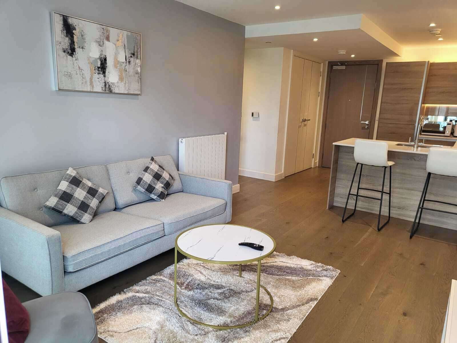 A modern living room with a grey sofa, a round coffee table, and a kitchen area with a bar stool.