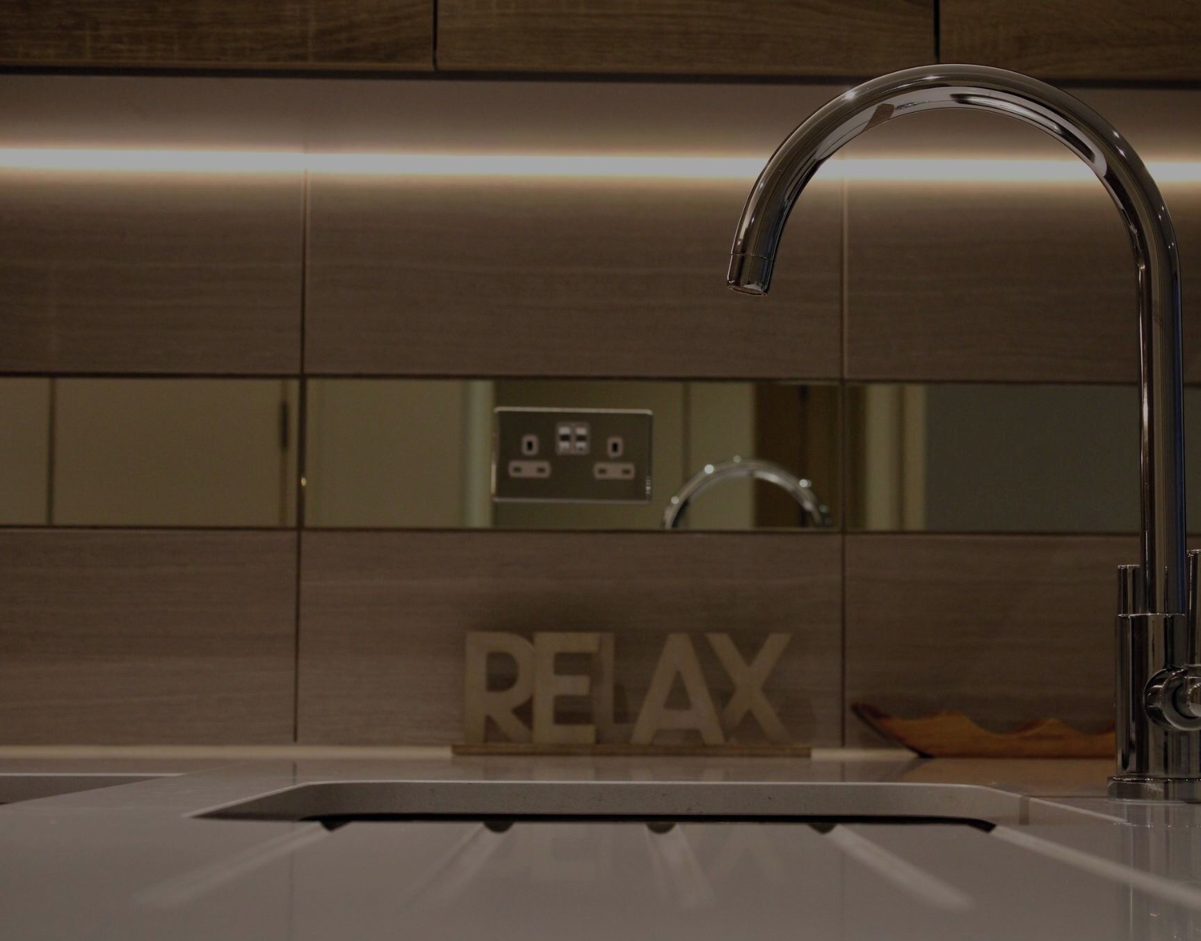 A modern kitchen with a sleek faucet, a built-in sink, and a control panel with a 'RELAX' sign.