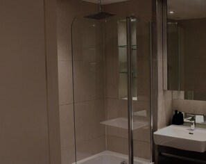 Ein modernes Badezimmer mit einer gläsernen Duschkabine, einem weißen Waschbecken und einem großen Spiegel.