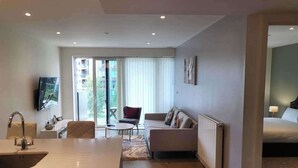 Ein modernes Hotelzimmer mit Küchenzeile, einer Couch, einem Esstisch und einem großen Fenster mit Blick auf die Stadt.