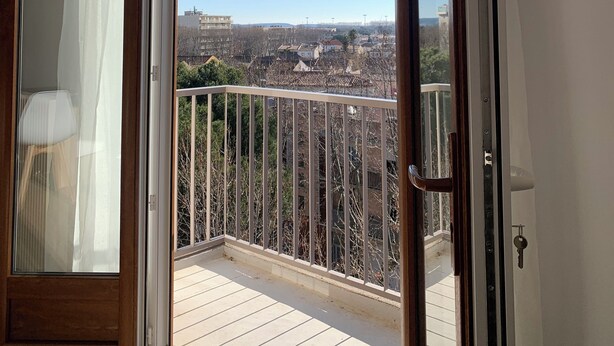 A balcony with a clear view of a residential area, a wooden door, and a white ceiling. - Panoramic view of Clape (Narbonne)