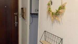 A hallway with a wooden door, a wall-mounted telephone, a decorative wreath, and a metal shelf. - Panoramic view of Clape (Narbonne)