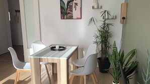 A modern dining area with a wooden table and white chairs, a painting on the wall, and several potted plants. - Panoramic view of Clape (Narbonne)