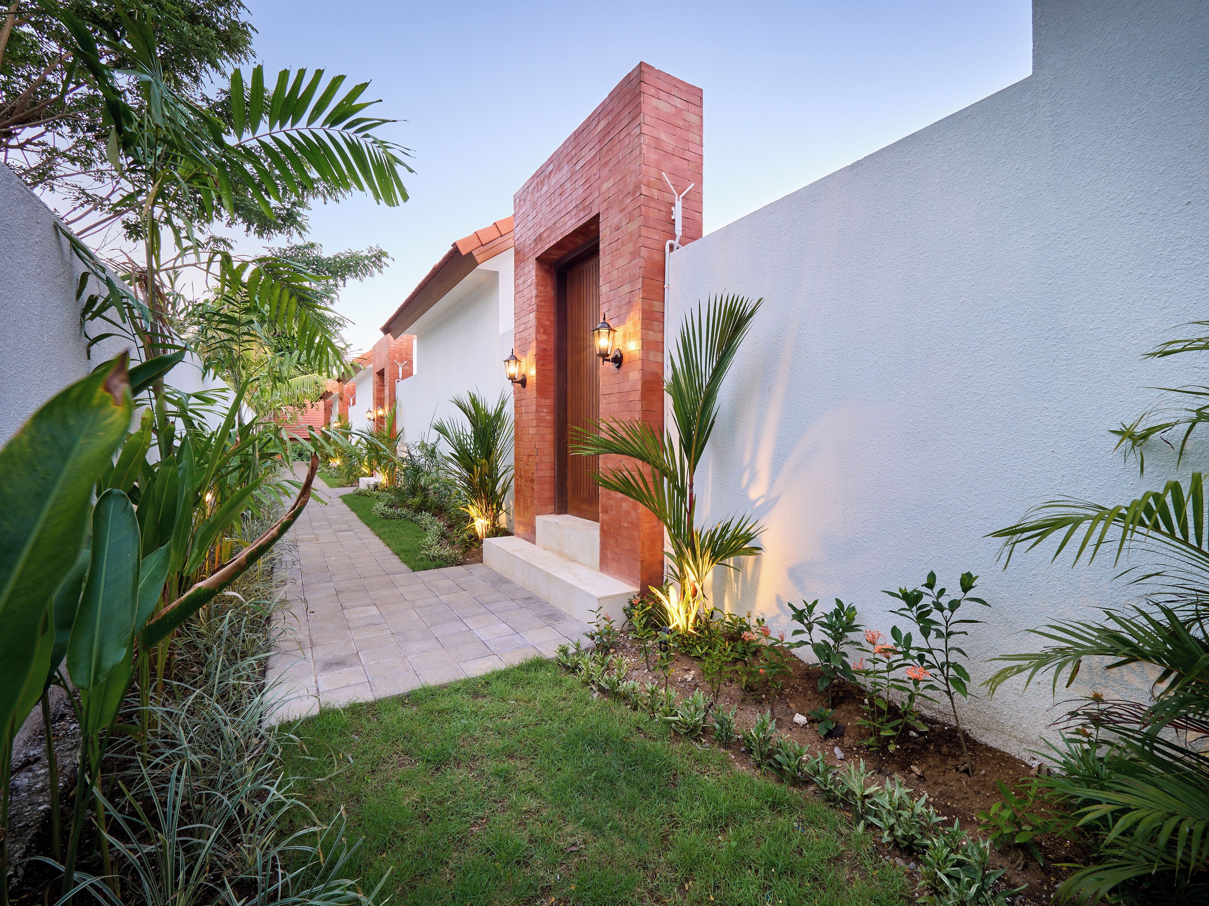 A modern building with a brick facade, a paved pathway, and lush greenery.