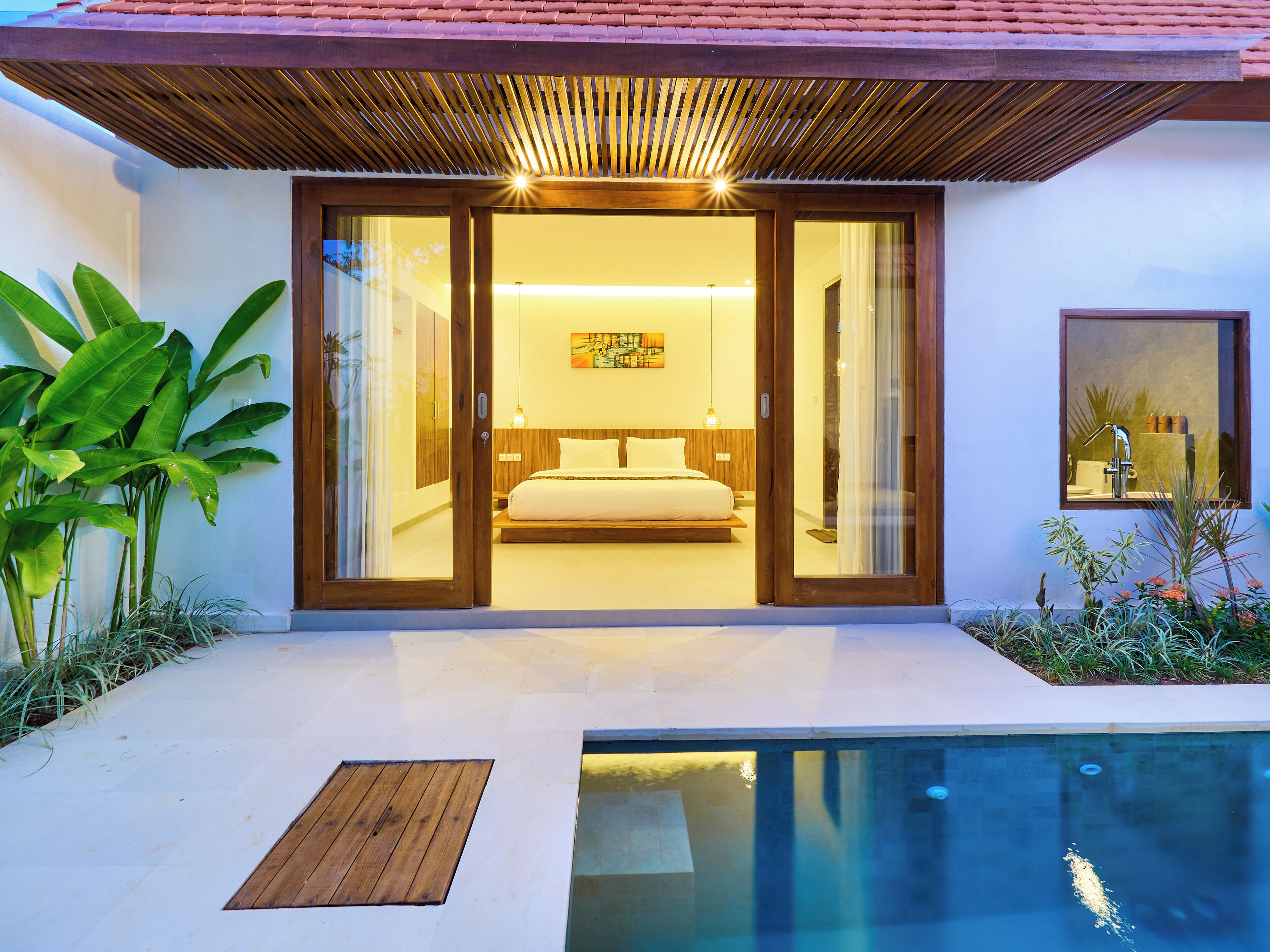 A modern bedroom with a large bed, sliding glass doors, and a view of a swimming pool.