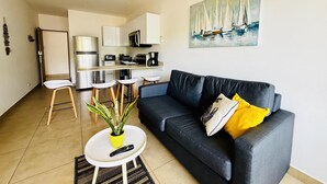 Een moderne woonkamer met een donkergrijze bank, een klein witte salontafel en een potplant. Een afstandsbediening ligt op de tafel.