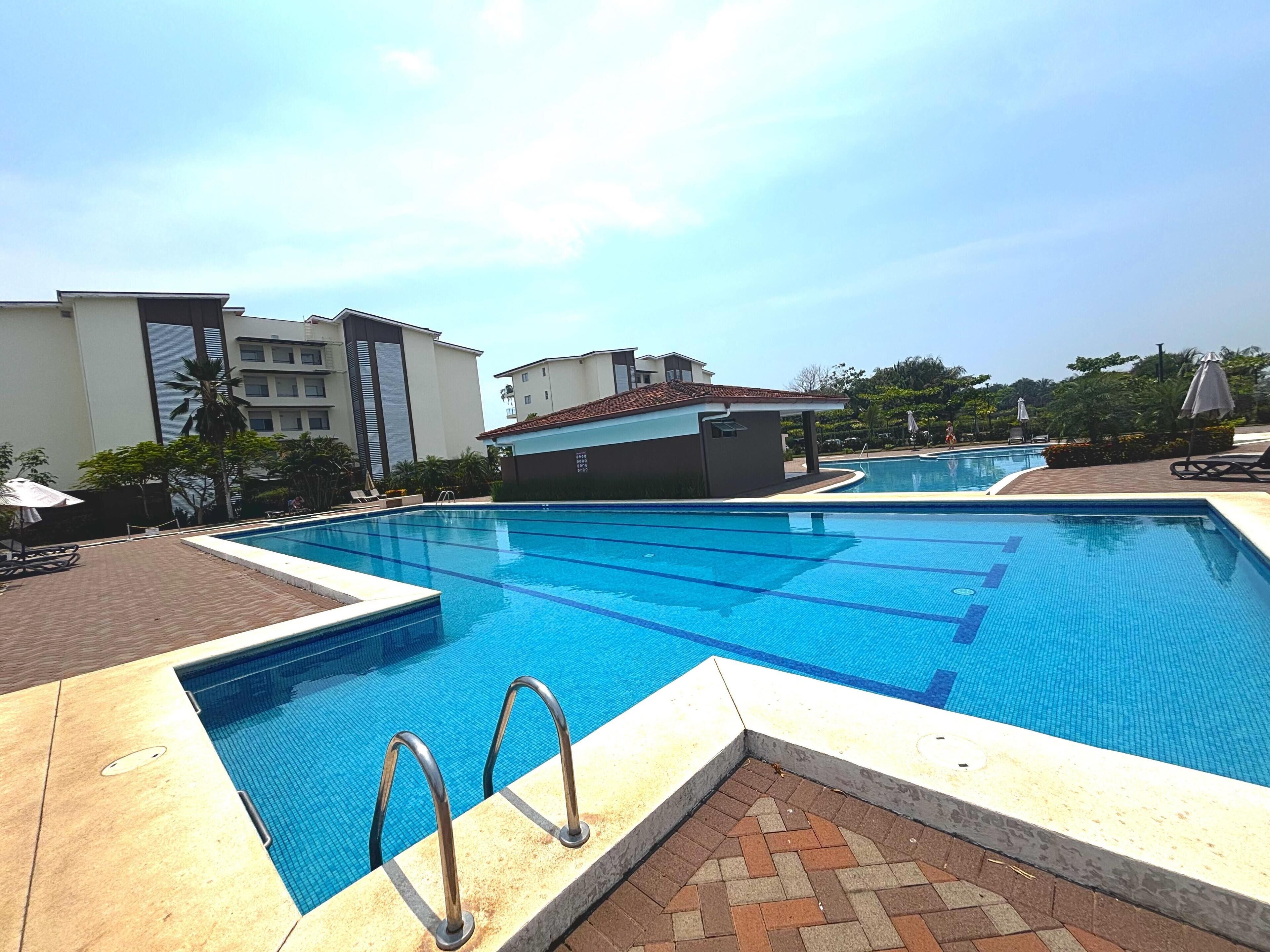 A swimming pool with clear blue water, surrounded by a brick deck and a tiled walkway.