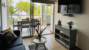 Een woonkamer met een bank, een salontafel, een televisie en een balkon met een tafel en stoelen.