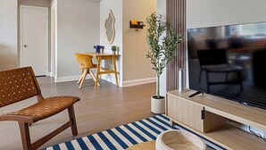 A modern living room with a sofa, a coffee table, a TV, and a dining area with a chair and table. - Arlington 1BR • Metro Access • Free Parking (Arlington)