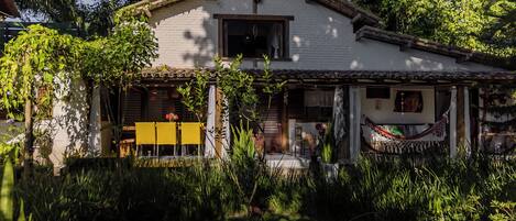 A white house with a tiled roof, surrounded by lush greenery and a hammock on the porch.