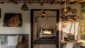 Un dormitorio con una cama, un banco, una lámpara colgante y un estante fijado a la pared con objetos decorativos.