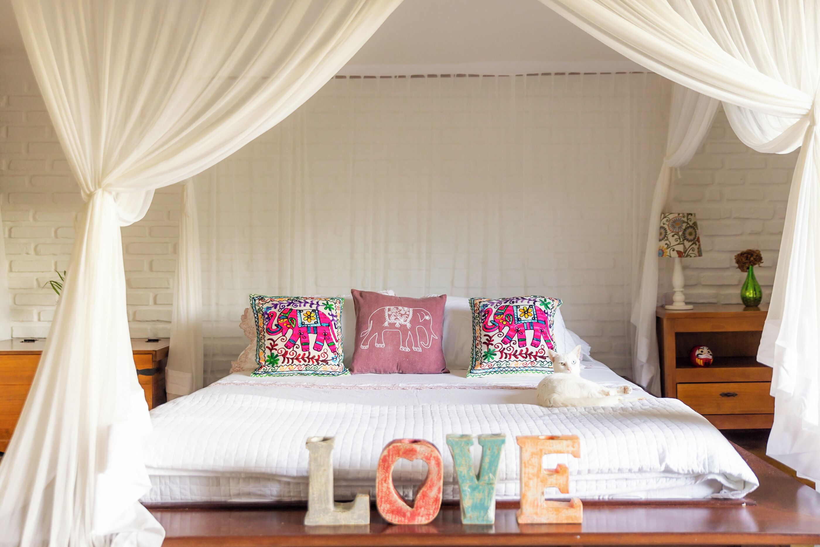 Una cama con dosel, almohadones decorativos y una mesita de noche con un florero.