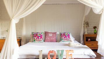 Una cama con dosel, almohadones decorativos y una mesita de noche con un florero.