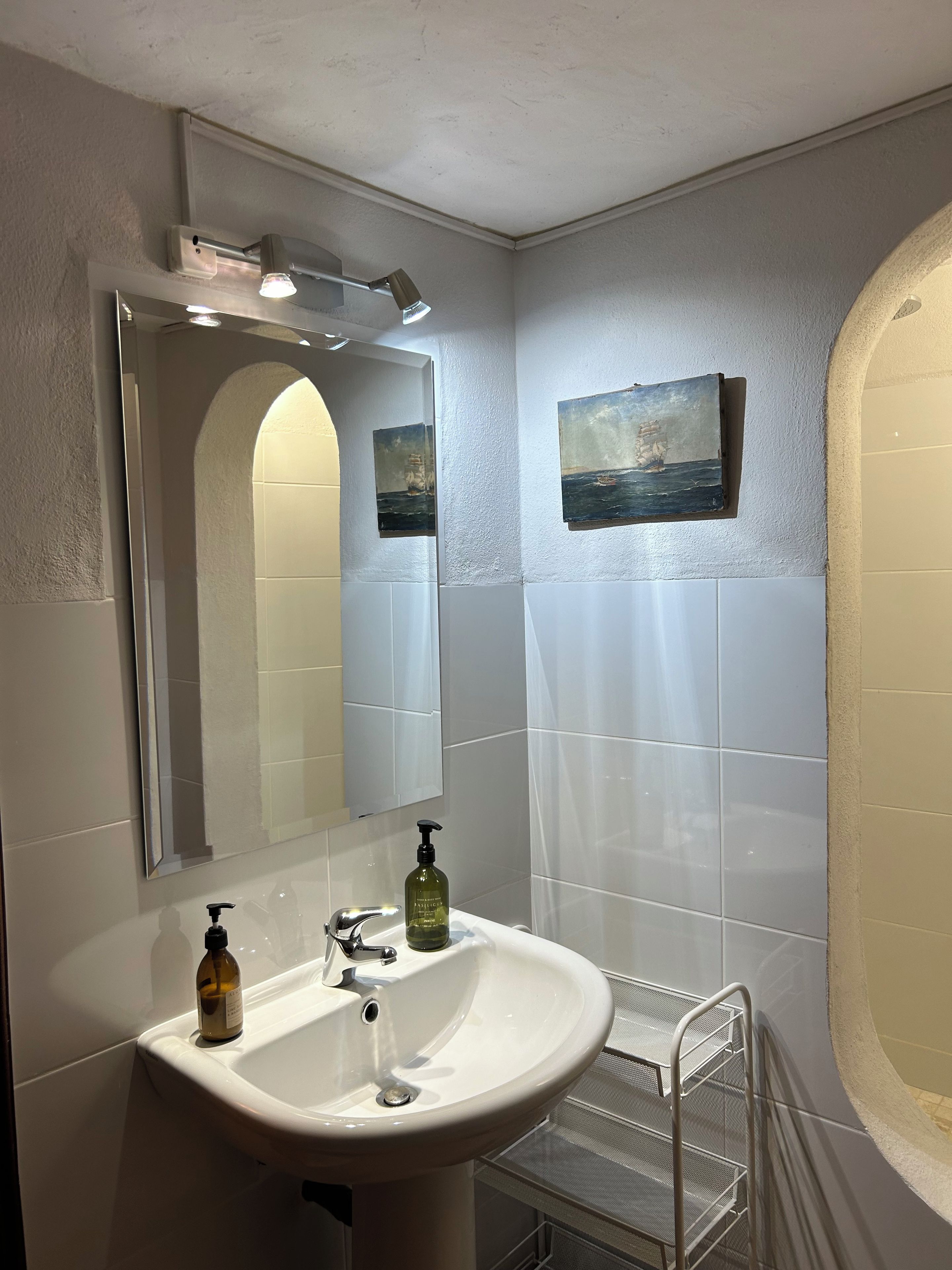 Une salle de bain avec un lavabo blanc, un miroir et deux tableaux accrochés au mur.
