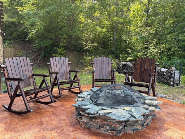 A patio with Adirondack chairs, a stone fire pit, and a wooden table. - Amazing Mountain and Lake Views! (Bryson City)