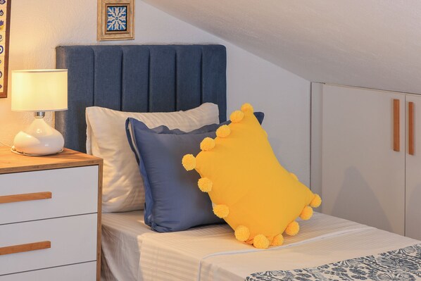 A bedroom with a bed, a nightstand with a lamp, a blue headboard, and a wardrobe.