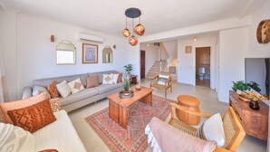 A spacious living room with a sofa, coffee table, and chairs. There is a staircase leading to another level.