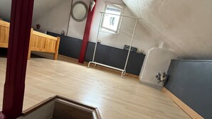Ett rum med ett sluttande tak, trägolv, en röd bjälkstruktur, ett fönster med utsikt och ett litet, runt föremål på väggen.