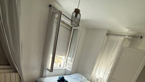 Ett sovrum med en enkelsäng, ett fönster med persienner, en hängande lampa och ett element.