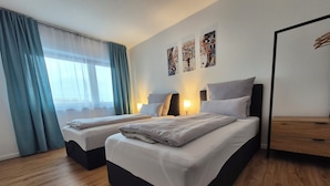 Een hotelkamer met twee bedden, een houten vloer, een raam met gordijnen en wanddecoratie.