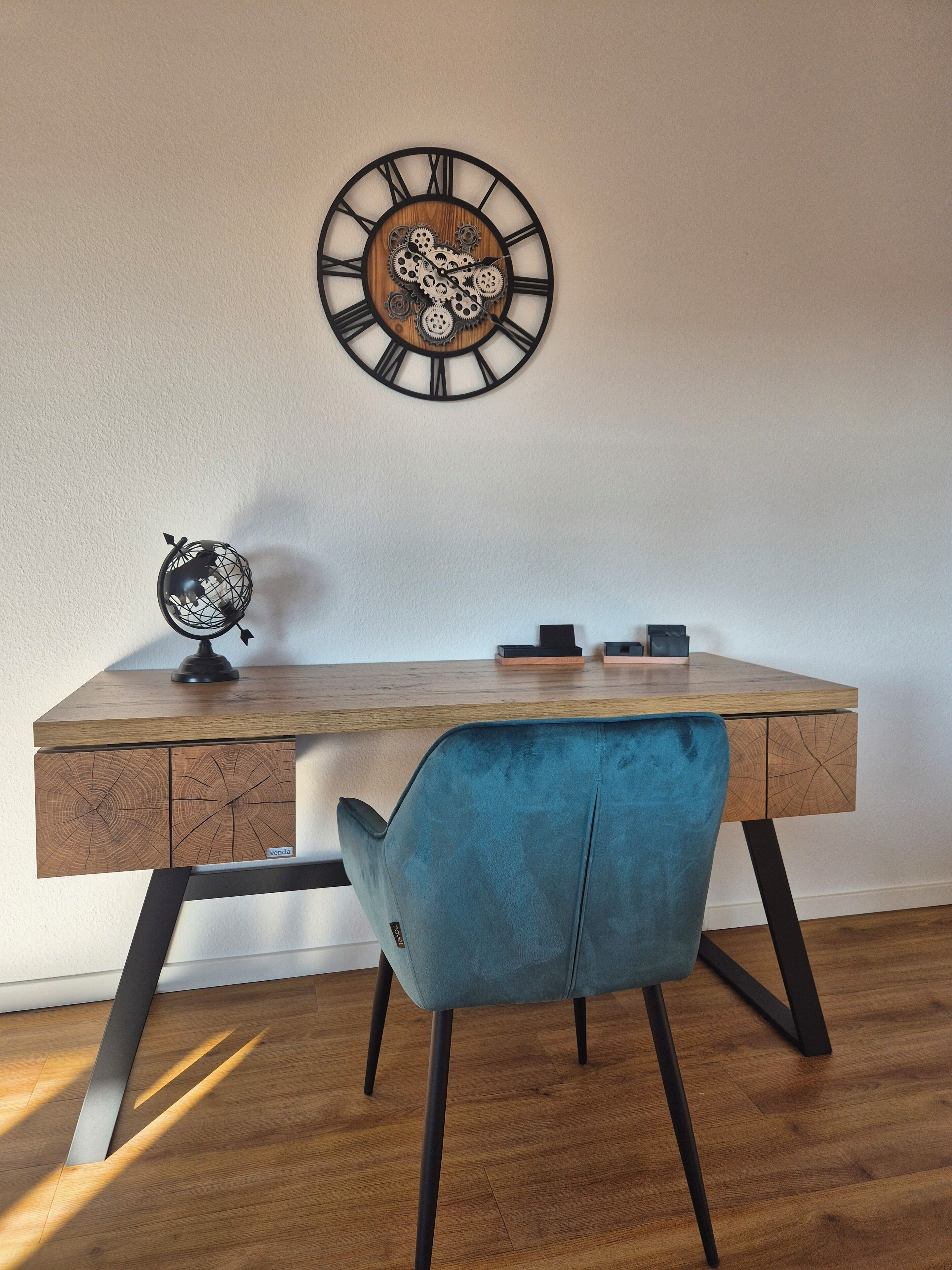 Un bureau en bois, avec une horloge, un globe terrestre et une chaise bleue, dans une pièce dont le sol est recouvert de planches de bois.