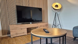 Een moderne woonkamer met een houten tv-meubel, een ronde salontafel, een afstandsbediening en een vloerlamp.
