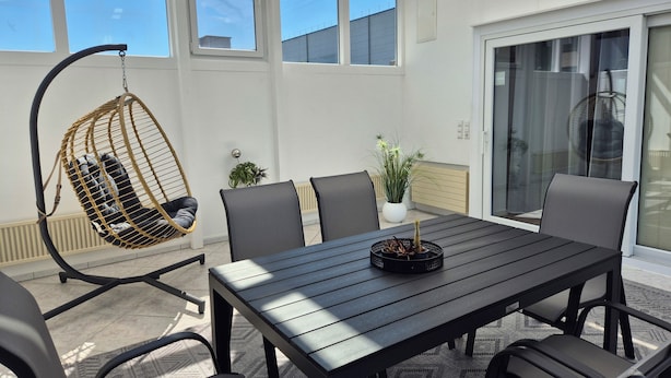 Een terras met een houten tafel, stoelen, een hangstoel en een bloempot.