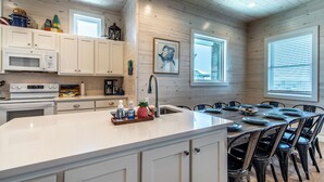 Una cocina moderna con armarios blancos, una isla central y una zona de comedor con sillas negras.