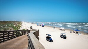 Una playa con un paseo marítimo de madera, sombrillas y carros de golf.